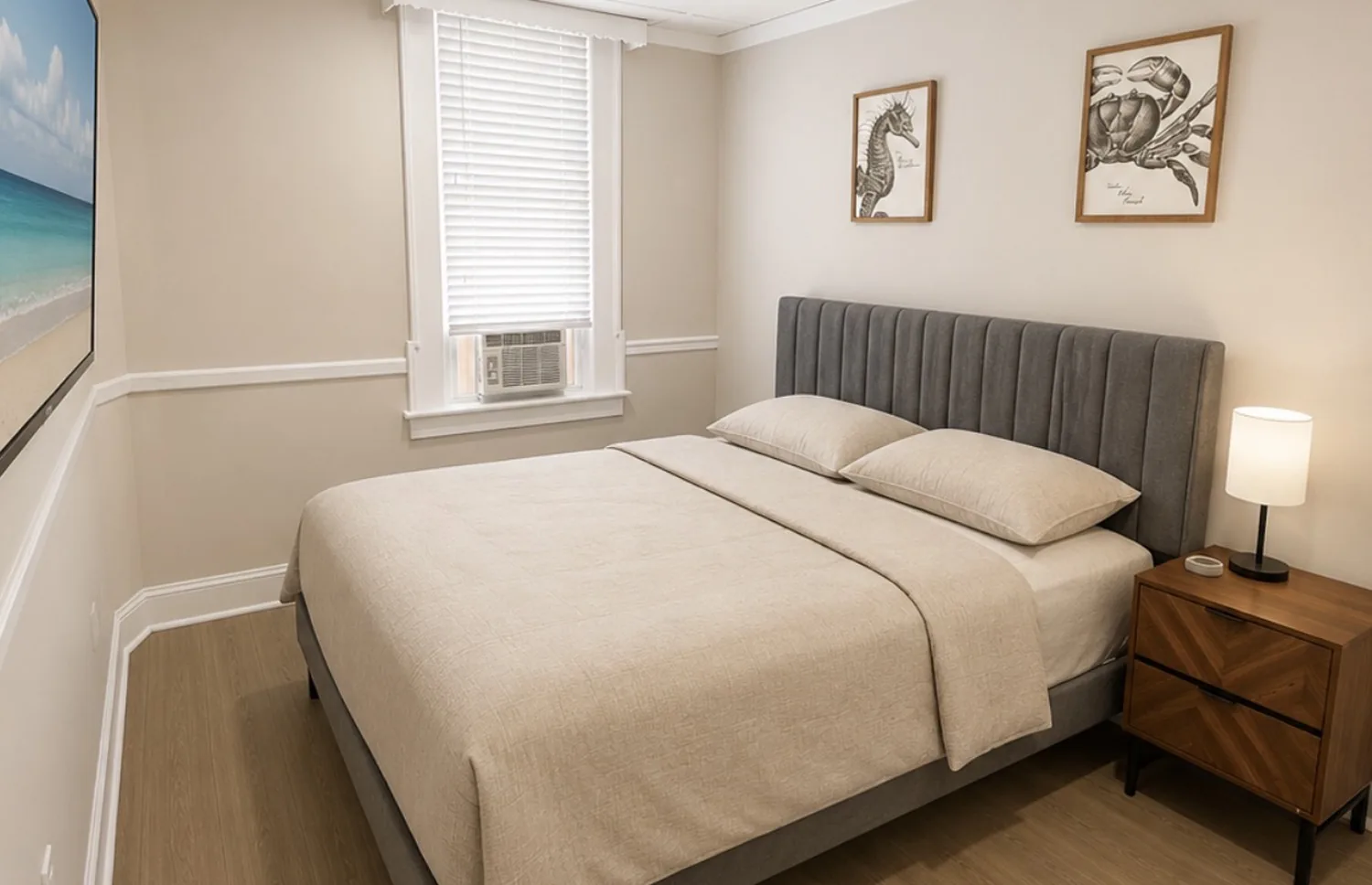 Private apartment bedroom with a beige bed, gray headboard, and coastal artwork